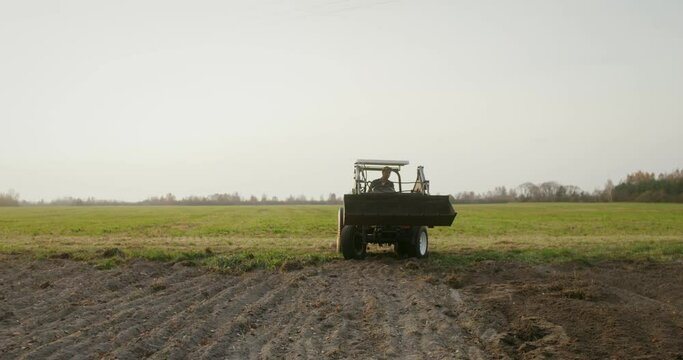 A male tractor driver drives an agricultural tractor plowing a small field