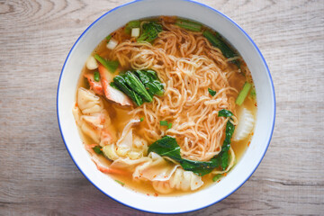soup noodle wonton pork yellow noodle with red roasted pork dumpling and bog choy chinese vegetable in soup bowl on wooden table, top view