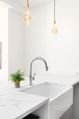 A kitchen sink detail shot with glass pendant lights hanging above the white granite countertop,...