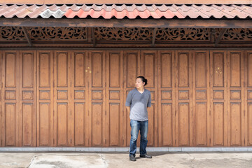 Fototapeta premium Asian long hair man is standing and posting in front of Classic backdrop wood wall and door in front of Thailand vintage traditional Building.