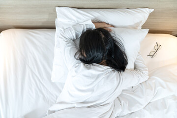 Asian Lady in white long arm t-shirt pajamas lie prone, lie on the stomach in bed with tried and...