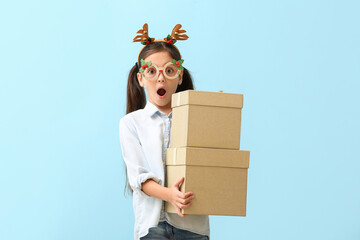 Funny little girl with reindeer horns and gifts on color background