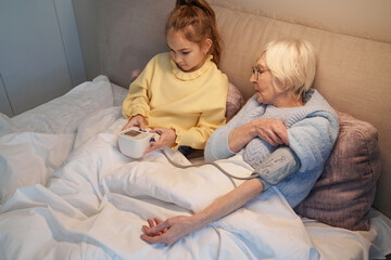 Concerned little girl checking her grandma blood pressure