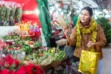 Cheerful asian woman customer buying traditional christmas bouquet at market in winter outdoors