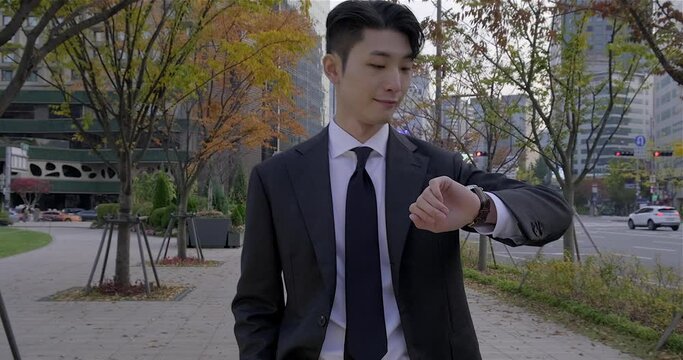 A good looking freshman walking down the street, checking the watch and wonder around in downtown Seoul city with autumnal background, bright and successful career.