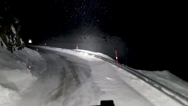POV Shot Of A Heavy Haul Logistics Truck Driving Up A Mountain Pass, Heavy Winds Pushing Snow Across The Tarmac Surface As The Driver Negotiates The Difficult Night Time Conditions In Norway, Europe 