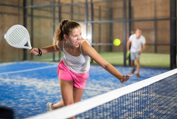 Young beautiful woman in white t-shirt playing padel tennis indoor