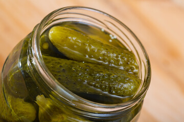 Image of opened glass jar with pickled cucumbers on wooden background