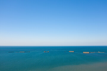 Obraz premium The artificial port of Gold beach in Asnelles in the middle of the English Channel in Europe, France, Normandy, Arromanches les Bains, in summer, on a sunny day.