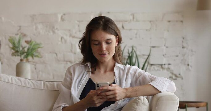Teenager relax on cozy sofa at home hold in hands cellphone smile enjoy sms chat with boyfriend, having pleasant distancing communication in social media with friend. Generation Z, modern tech concept