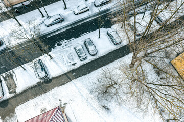 snow-covered trees and cars on parking lot. winter season in city. aerial top view from flying drone.