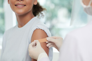Close-up image of nurse sticking adhesive plaster on arm of teenage girl after injecting vaccine...