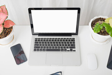 Modern workspace, mock up laptop computer blank white screen, eyeglasses and smartphone white table have potted plants on the desk, Notebook and mobile phone on desktop home office