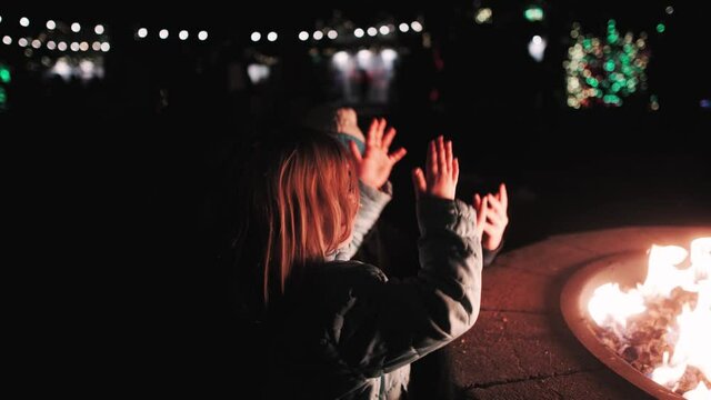 Mother and daughter warm their hands over a firepit at a Christmas festival - cute three-year old toddle looks at camera