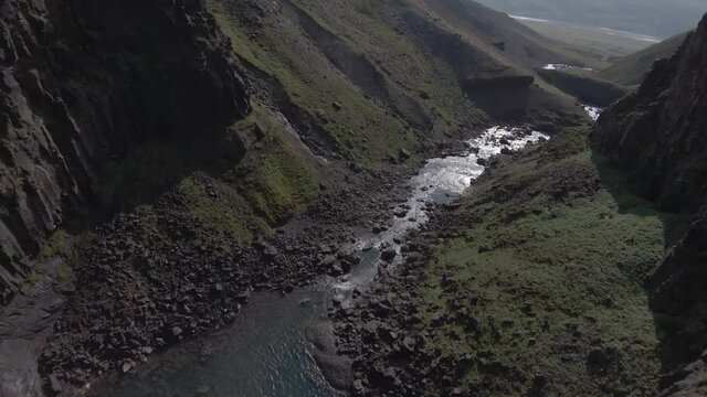 Dive bombing past waterfall in Iceland canyon with bright sunlight, FPV Shot