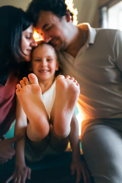 Happy parents hug their daughter, she sits with her legs outstretched. Front view.