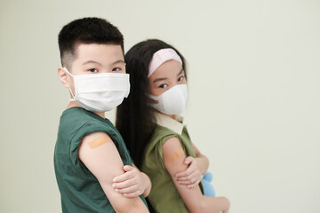 Kids in medical masks showing shoulder with adhesive plasters after they got vaccinated against coronavirus
