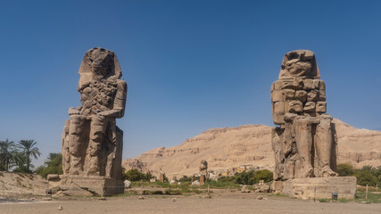 Giant ancient statues of the colossi of Memnon rise in the valley. Huge figures of sitting people...