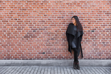 Asian young woman fashion model standing on street against brick wall background wearing winter wool coat and elegant dress for work.