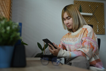 Smiling asian woman using smart phone while sitting in her home office.