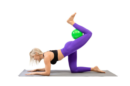 Exercise leg kicks with small fit ball. Athletic beautiful woman stand on all fours on a mat and practice pilates with props, isolated on white.