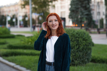 Fototapeta premium Portrait of a young, beautiful and attractive redhead Caucasian girl with freckles. Girl posing walking through the city.