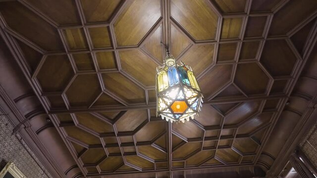 Bottom view of a wooden beautiful old fashioned ceiling with a hanging chandelier made of stained glass. Action. Details of a retro stylized room or a museum.