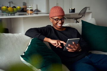 Black adult male typing on tablet in the lounge of modern apartment. Smiling