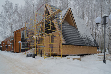Winter construction of a small house. Wooden materials are used. There are scaffolding.