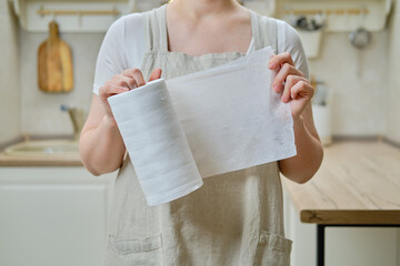 A woman holds a roll of cloth towels in her hands while standing on a home kitchen, close-up