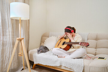 A confused crying woman plays an acoustic guitar sitting on a bed in a home living room