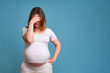 Pensiveness on face of pregnant woman, studio shot on blue background