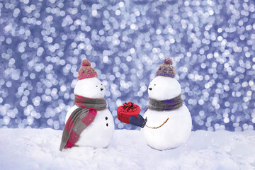 Snowmen in love wearing winter hats, scarves on a white background. Boy giving a gift to his girlfriend. Christmas, Valentins day, love concept. 14th february. Copy space. Trendy color of the year
