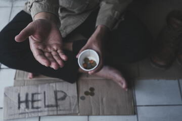 Homeless adult man sitting on the street in the shadow of the building and begging for help and...