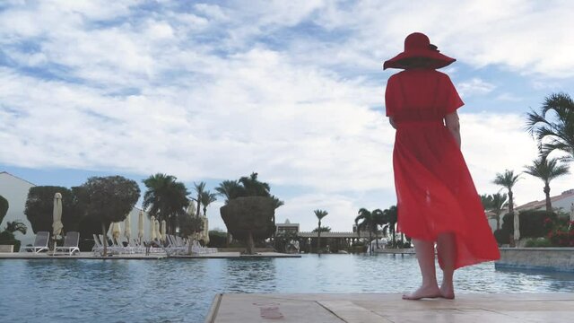 Summer vacation woman in red hat and cape for the beach with mobile phone near swimmimg pool amd palms, woman blogger