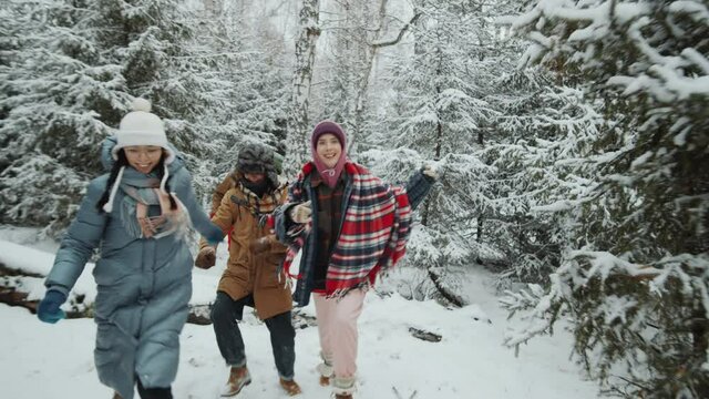 Joyful young friends smiling and running through snowy forest while having fun outdoors on winter day