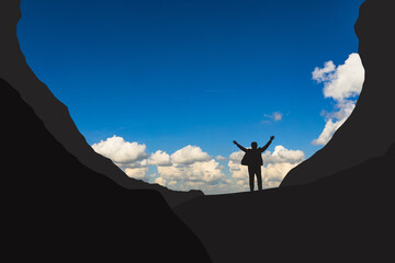 silhouette of a business man standing with his hands up in the mountains