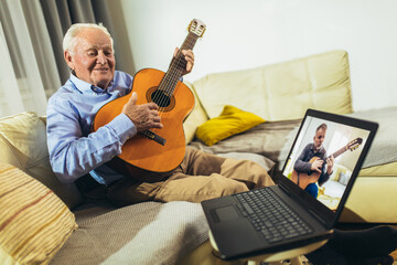 Senior man playing guitar at home using laptop for online lessons