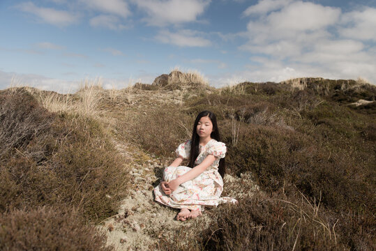 romantic portrait of young woman sitting on the grass in classic floral dress in dunes 