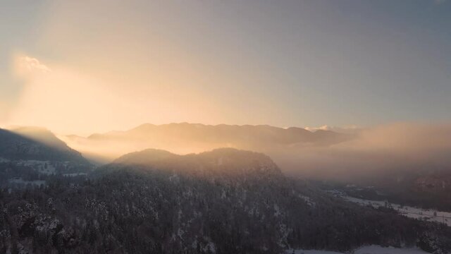 Drone shot of a mysterious landscape at sunset in the mountains covered with clouds in wintertime