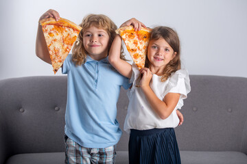 Happy daughter and son eating pizza. Children kids enjoy and having fun with lunch together at home. Funny children eating pizza and having fun together, holding pizza slice near face.