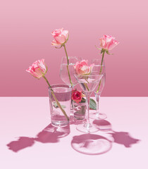 Roses placed in clear water glasses of all shapes and sizes, set against pink background.
