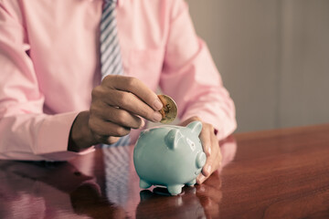The hand of a businessman puts coins in a piggy bank, saves money with coins, steps into a...