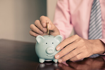 The hand of a businessman puts coins in a piggy bank, saves money with coins, steps into a...
