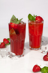 Two glasses of iced strawberry drinks with basil and mint