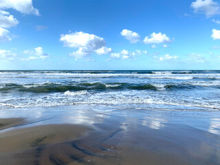 The sea coast with the reflection of white clouds on the sand
