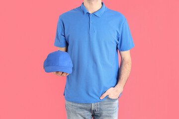 Man in blank blue polo holds cap on pink background