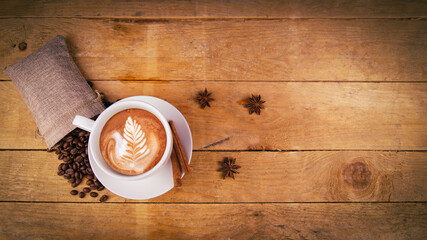 Coffee cup top view on old wooden table. Leaf pattern on cafe latte. Anise stars, coffee beans in...