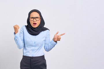 Portrait of shocked young Asian woman pointing fingers at copy space with victory gesture isolated on white background