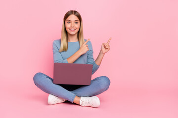 Full body photo of young girl indicate fingers empty space banner select use laptop sit floor isolated over pink color background